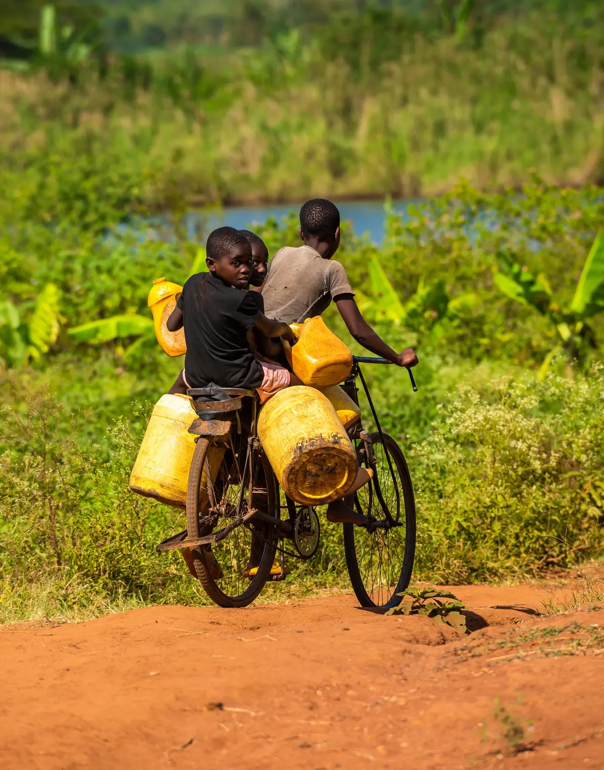 A boy rides a bicycle carrying water containers and his younger brothers  searching for water